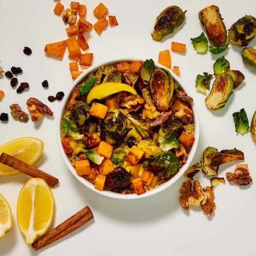 Roasted Brussels Sprouts Bowl surrounded by its ingredients: Brussels sprouts, butternut squash, walnuts, currants, lemon, and cinnamon