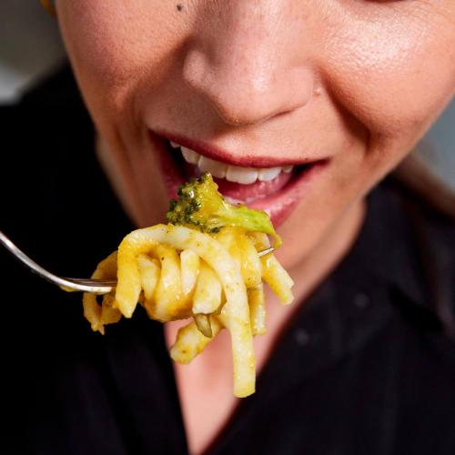 A close-up of Creamy Butternut Squash Noodles twisted on a fork near a woman's mouth.