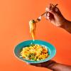 Creamy Butternut Squash Noodles in a dish being held by a woman on an orange background.