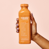 Hand holding carrot ginger chia smoothie on pink background. 