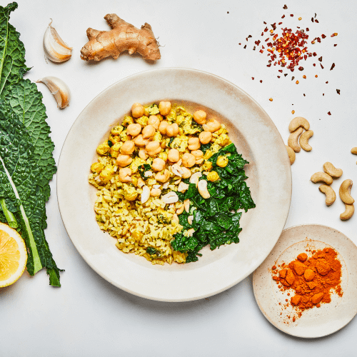 COCONUT CURRY RICE BOWL ON WHITE SURFACE WITH KALE, LEMON, CASHEWS, CURRY POWDER, GINGER, GARLIC AND CRUSHED RED PEPPER FLAKES. 