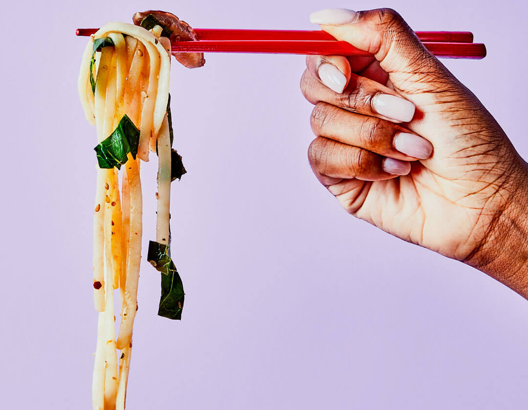Person holding noodles up with chopsticks