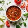 Garden Minestrone Soup in a white bowl surrounded by its ingredients: tomato, zucchini, basil