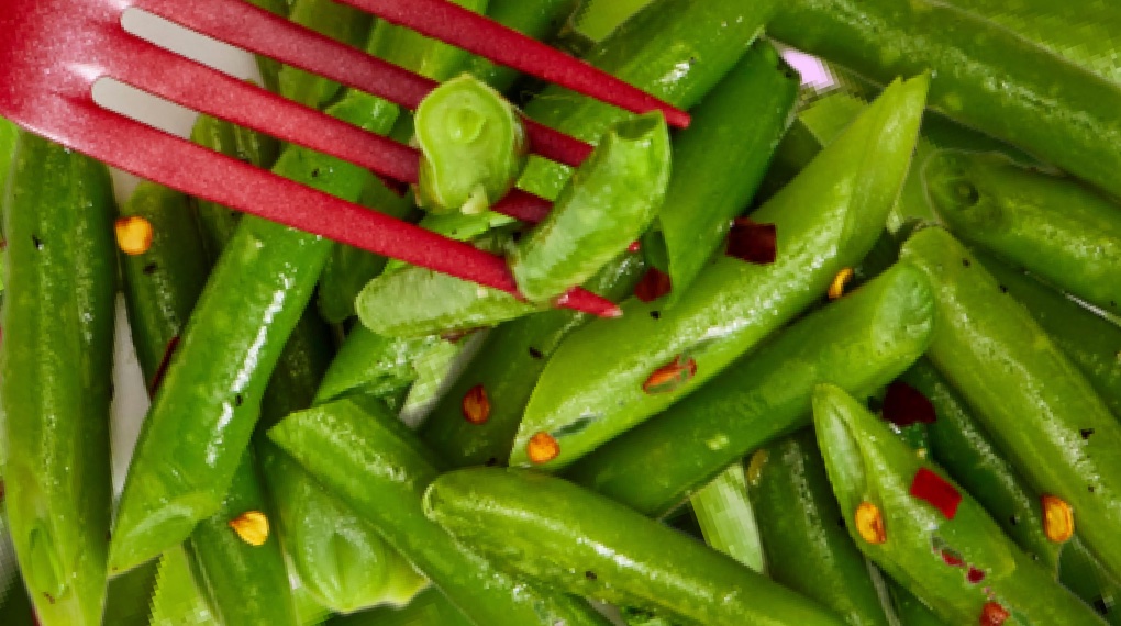 A close-up of a red fork scooping up green beans