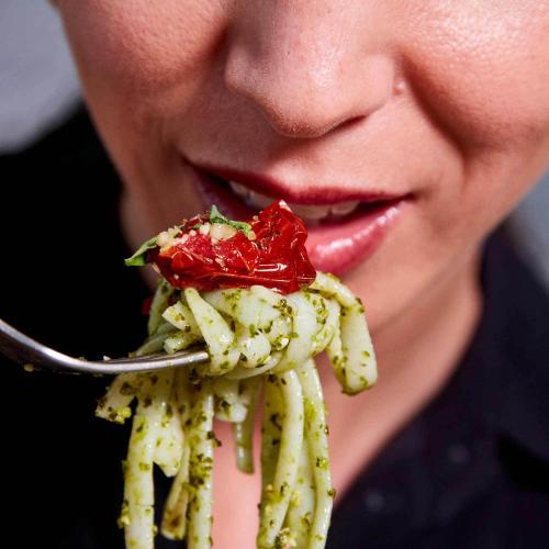 A close-up of Kale Pesto Noodles twisted on a fork near a woman's mouth.