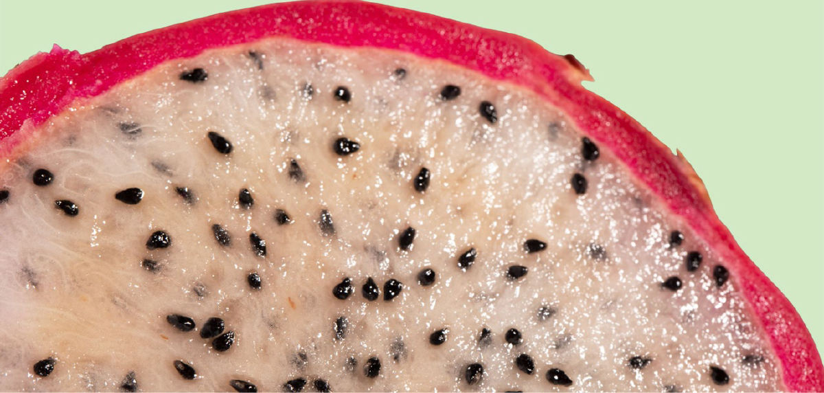 Close up of a dragon fruit that has been sliced in half. The top  of the image shows the red skin of the fruit, and the majority of the image shows the flesh.