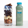 A clear cup filled with Blue Majik Smoothie ingredients: almonds, bananas, dates, coconut, blue spirulina powder, and cinnamon sticks.