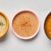 Cauliflower Potato Chowder Soup in yellow bowl, parsnip apple puree in pink bowl, pumpkin pear bisque in blue bowl on white background.