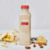 Sliced banana, bottle of banana flax smoothie, almonds, flax seeds and lemon on a white background. 