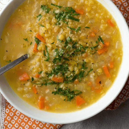 Red Lentil Dal Soup IN WHITE BOWL WITH SILVER SPOON ON AN ORANGE AND WHITE NAPKIN.