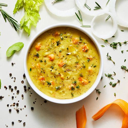 Red Lentil Dal Soup in a white bowl surrounded by its ingredients: celery, onions, thyme, Carrots, and black pepper