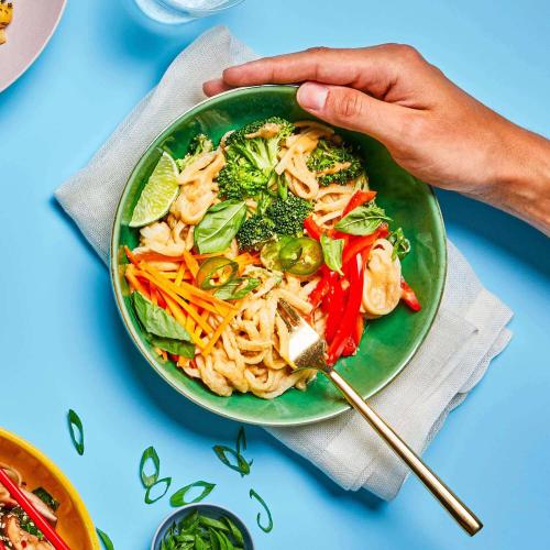 Tangy Ginger Noodles in a dish with a fork in it, on a table with a few other dishes and a napkin.
