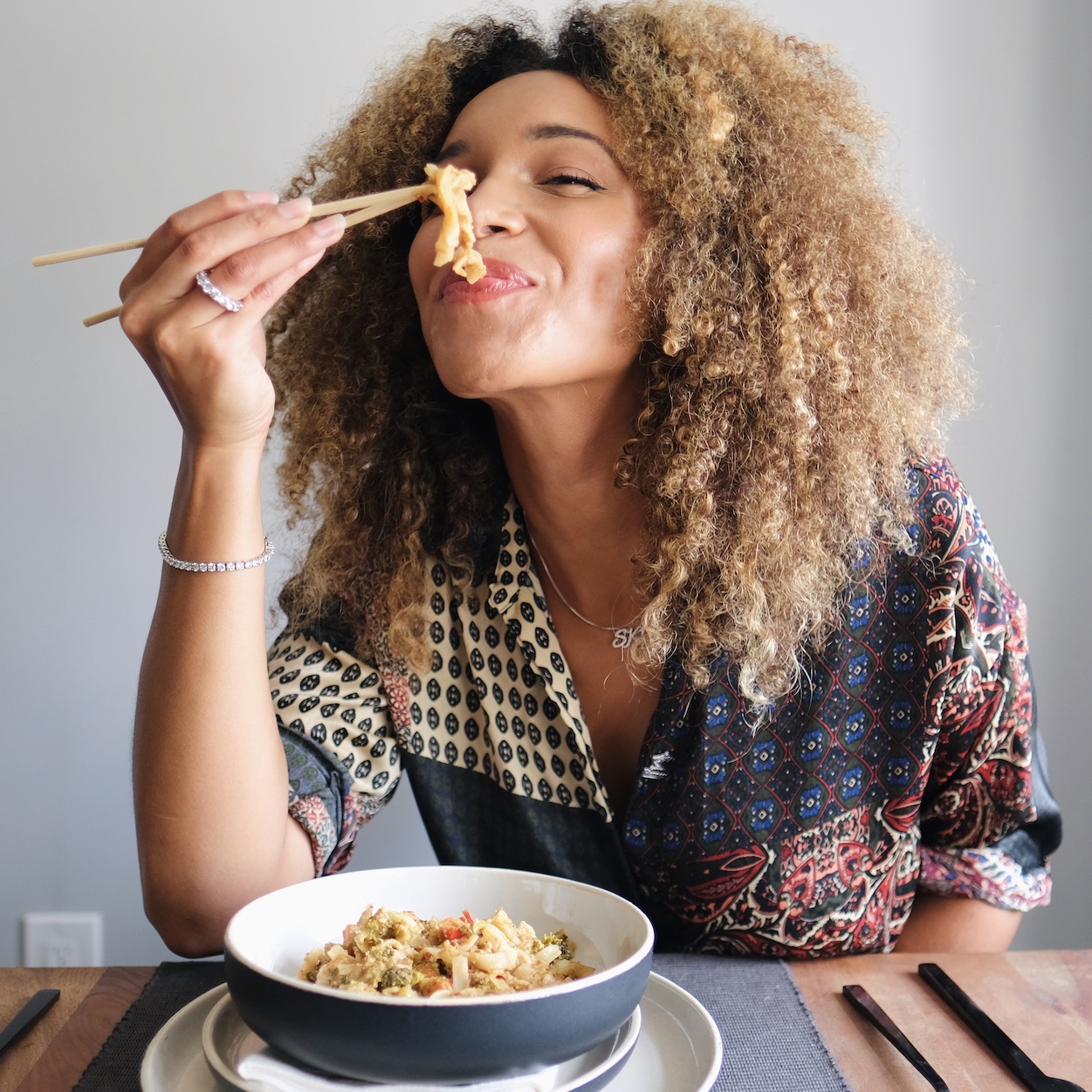 The social media personality Sky Landish smiling and holding a noodle with chopsticks while sitting at a table