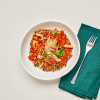 Vegetable bolognese in white bowl, on white background with teal napkin and silver fork.